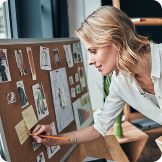 Woman holding a pencil and writing on a sticky note that is on her bulletin board.