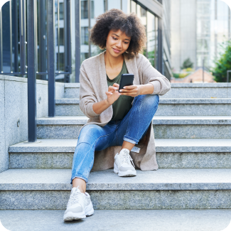 Woman sitting on stairs outside while looking at her phone and smiling.