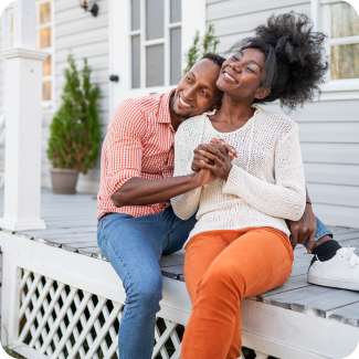 Young couple sitting on the front porch of their home smiling while embracing each other.