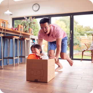 Father pushing his son around in a box in their kitchen.