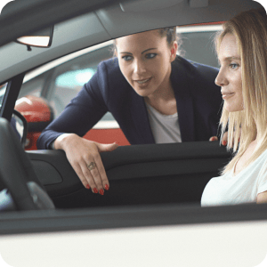 Woman sitting in a car talking to the car sales woman.