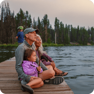 Grandparents sitting with granddaughter on a dock.