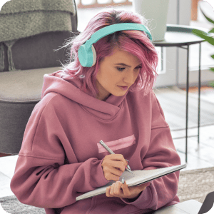 Girl with pink hair writing in a notebook.