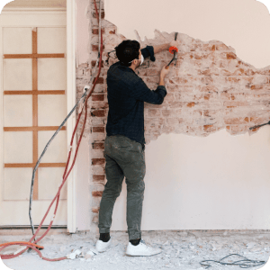 Man scrapping old wall off brick in his home.