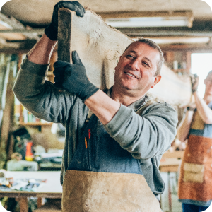 Carpenter carrying a large slab of wood around his shop.