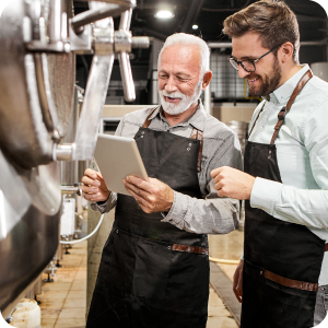 Two male beer brewers conversating over a formula in their brewery.