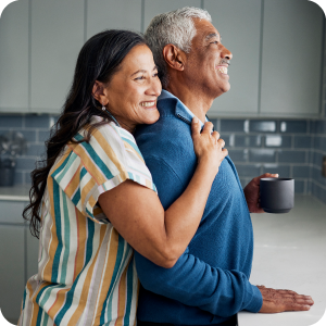 Mature couple embracing each other in a hug in their kitchen while looking our the window.