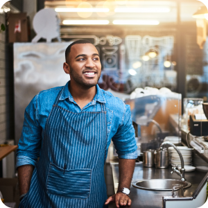 Man wearing an apron while standing in a commercial kitchen by the sink.