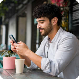 Smiling man looking at his cell phone while sitting at a picnic table by a restaurant.