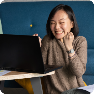 Happy woman sitting on the floor while using her laptop on a small table.