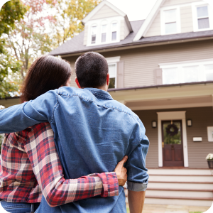 Married couple embracing each other outside of their new home they just purchased.