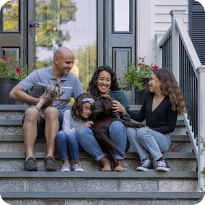 Happy family sitting on the front steps of their home cuddling their dog.