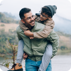 A father giving his son a piggy back ride outside near a lake.