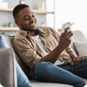 Man sitting on a couch looking at his cell phone and smiling.