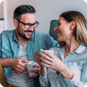 Married couple looking at each other and smiling while drinking coffee.