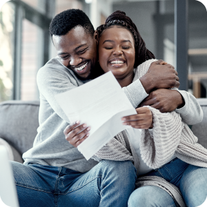 Couple very happily embracing while sitting on a coach as they look at a loan approval paper.