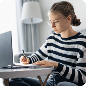 Teenager writing and looking at a laptop.