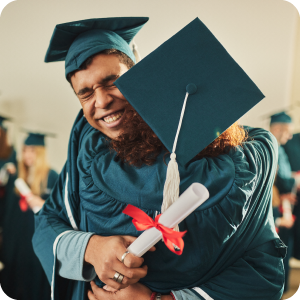 Two friends who just graduated hugging each other while holding their diplomas.