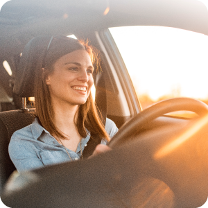 Woman happily driving her car with the sun shining through the window.